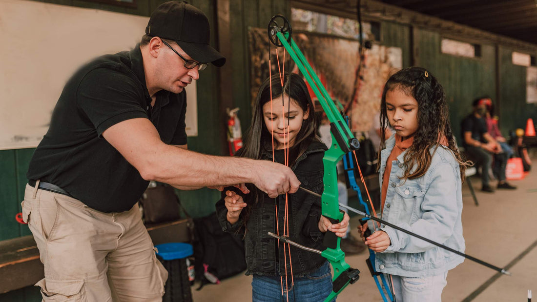 Child shooting a youth compound bow at an outdoor range.